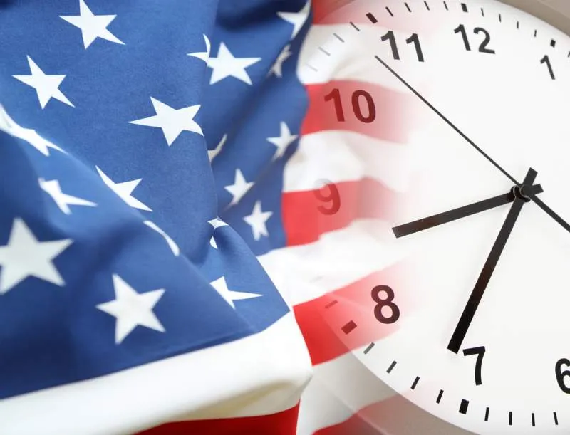 American flag fading into an analog clock with a white face and black numbers and hands.