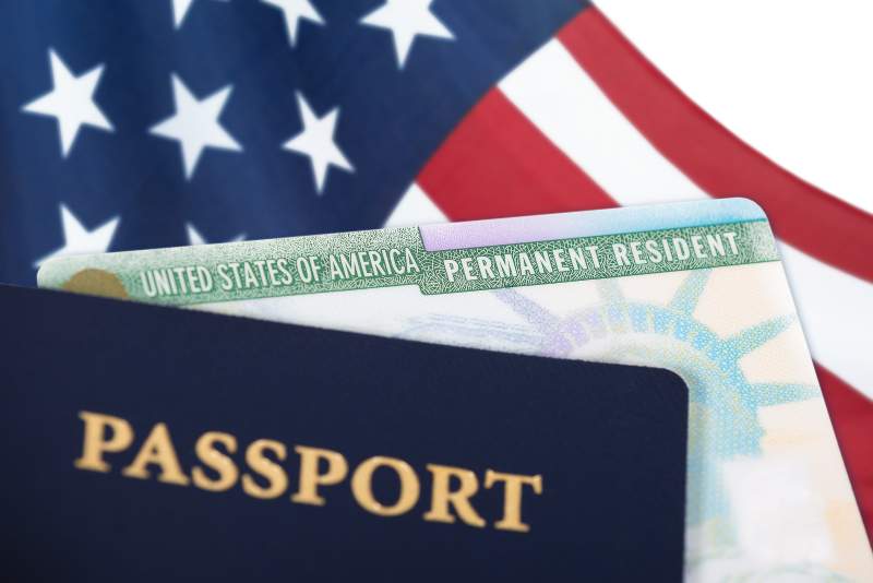 united states flag behind green card and passport