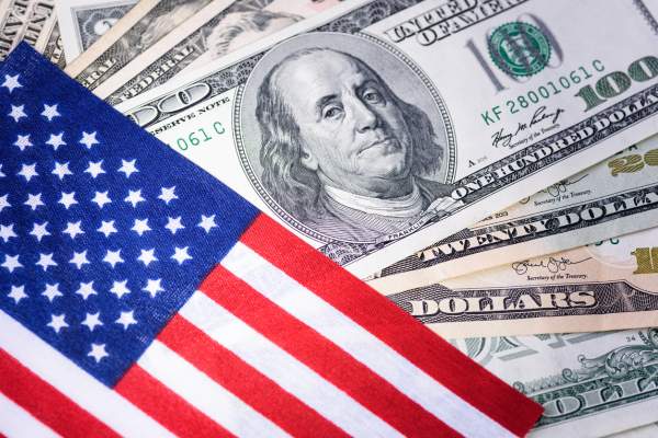 One-hundred-dollar bills next to an American flag