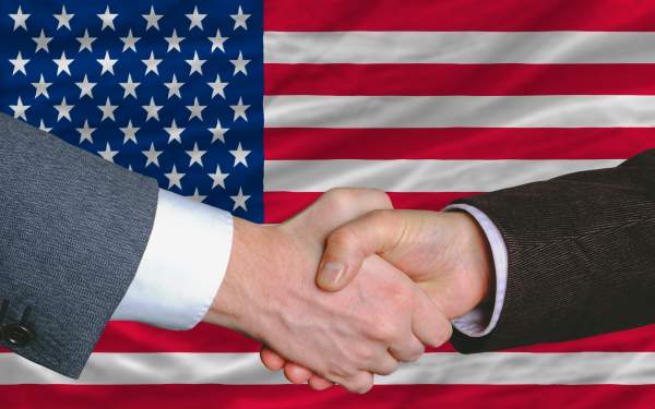 closeup on two business people shaking hands in front of american flag