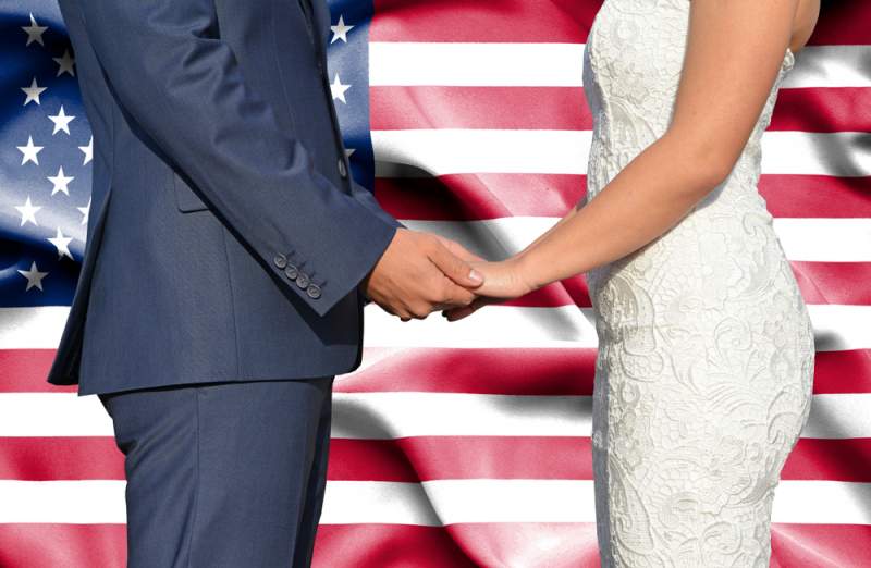 couple holds hands at wedding in front of american flag