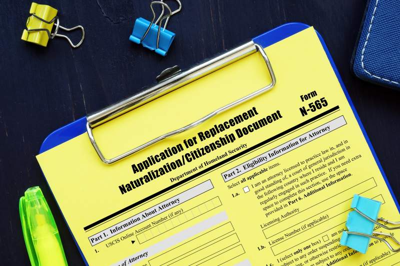 Clipboard with yellow N-565 document on a dark table with colorful paper clips.