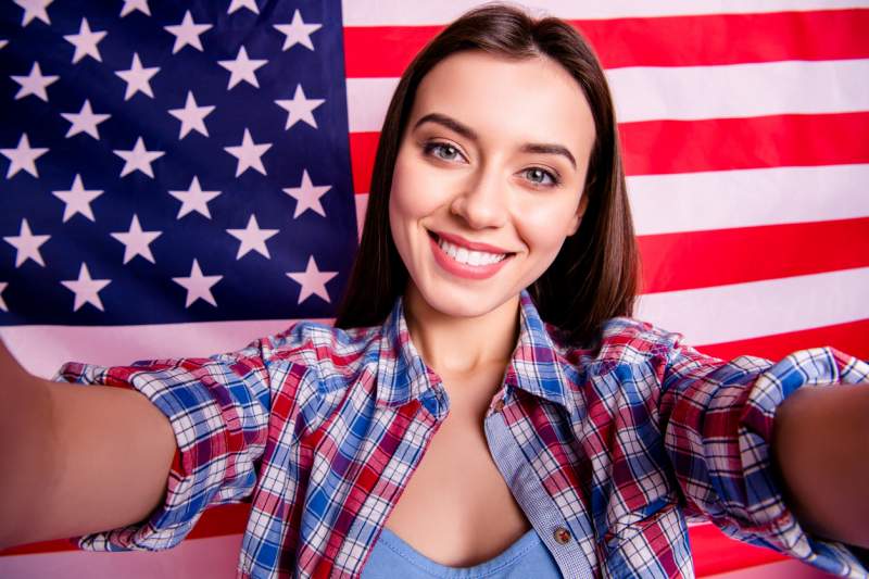 woman takes selfie in front of american flag