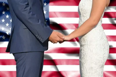 A bride and groom holding hands facing each other in front of the United States flag.